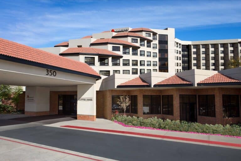 A multi-story hotel with a beige facade, red-tiled roofs, and a visible “Marriott” sign. The building is surrounded by landscaping and a driveway, with the street number 350 displayed above the entrance.