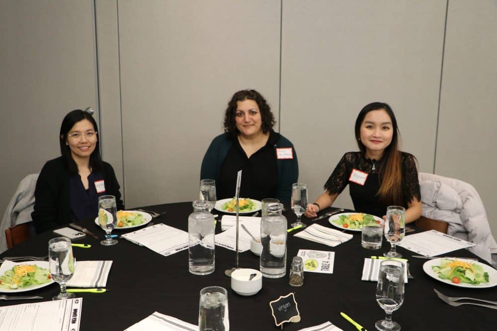 Three event attendees seated with vegan-labeled meal options at the table