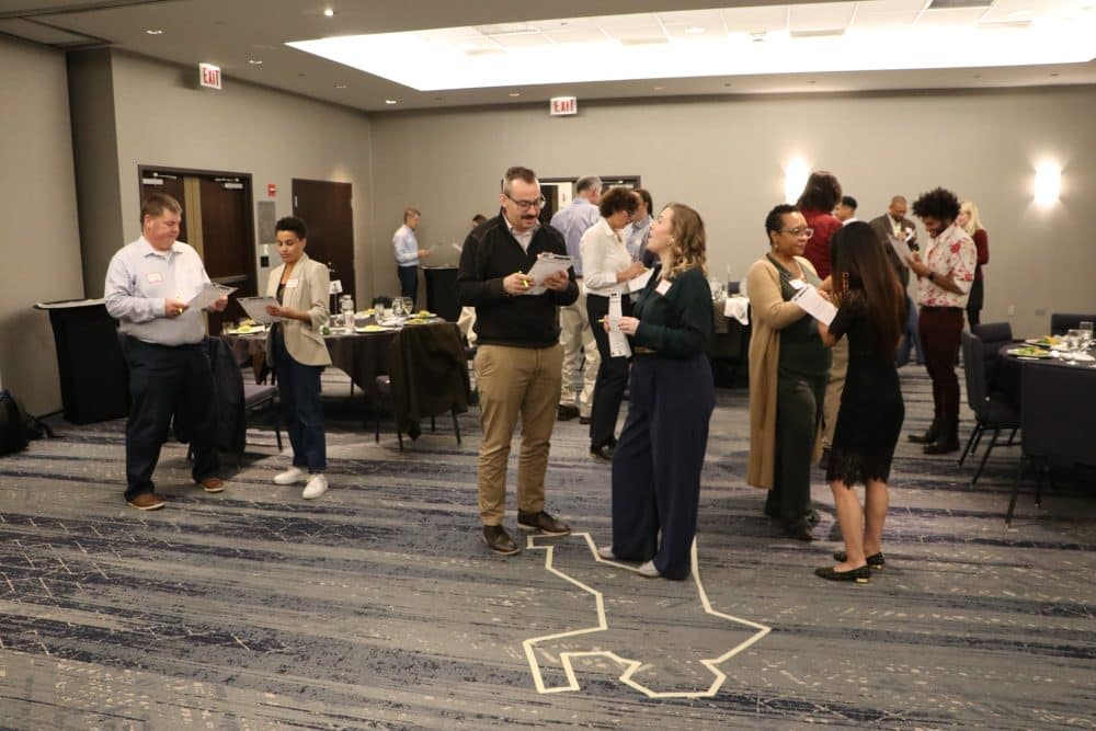 Corporate event participants engaging in a mystery-solving challenge near a taped body outline.