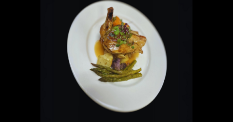 Elegant plate of roasted chicken with gravy, potatoes, and green asparagus on a white plate.