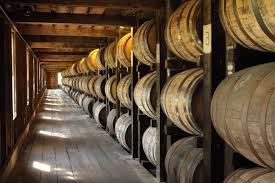A dimly lit warehouse interior in Lexington, KY, with rows of wooden barrels stacked on racks. Sunlight filters through small windows, casting soft light on the smooth, aged barrels. The floor is wooden, and the atmosphere is rustic and vintage—a unique thing to do in Lexington KY.