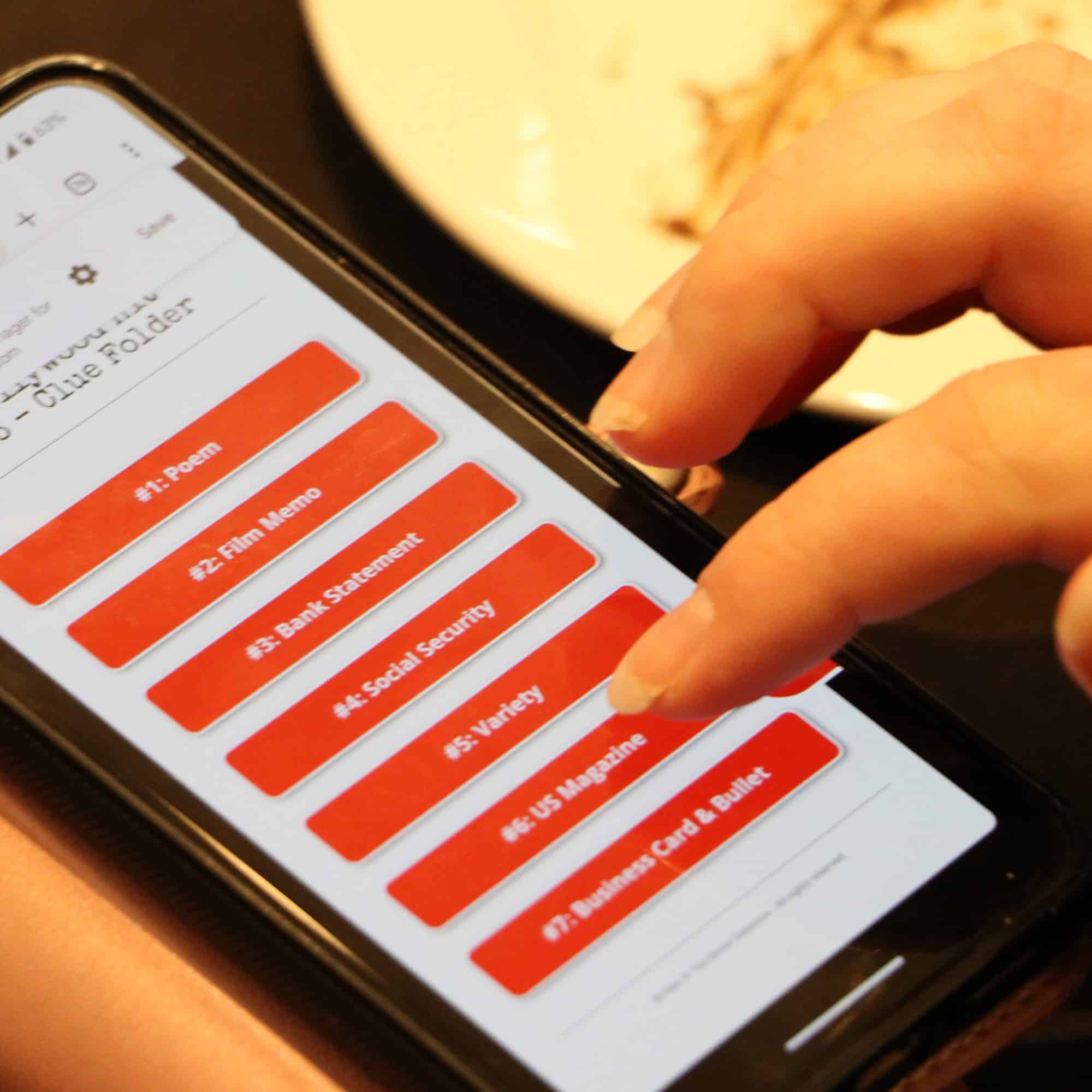 A person is using a smartphone, navigating a web page with a list of red buttons labeled with various tasks like Film Videos, Bank Statement, and Social Security. A white circular plate is partially visible in the background.