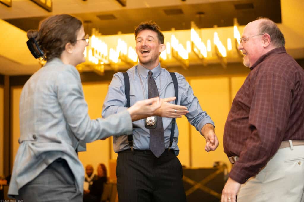 Dinner Detective performer in detective attire interacting with two audience members during a live Lexington murder mystery show