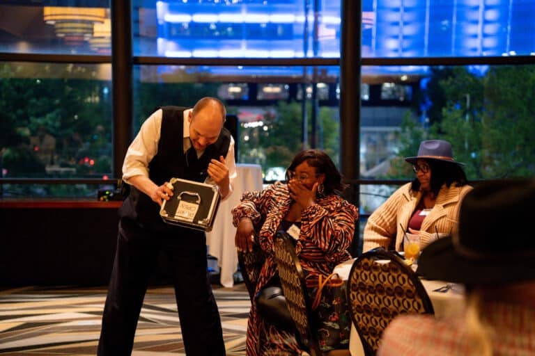 Guest reacts with surprise as a Dinner Detective actor presents a mysterious case labeled "Do Not Open" during an interactive murder mystery dinner in Lexington KY
