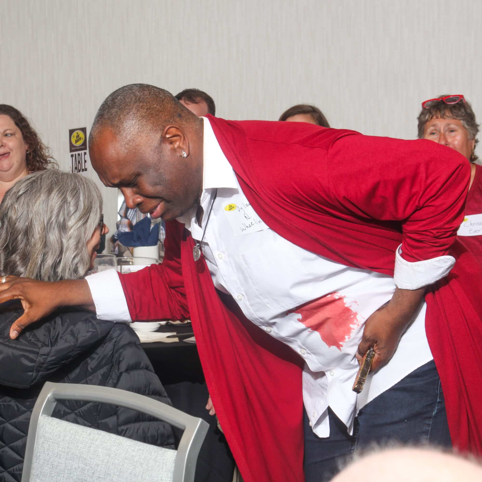 A man in a red robe clutches his side, pretending to be wounded during an interactive moment at The Dinner Detective Murder Mystery Show in Louisville.