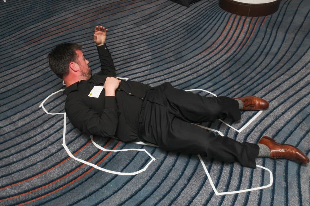 A man in black lies in a mock crime scene chalk outline at The Dinner Detective Murder Mystery Show in Louisville.