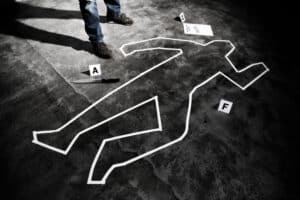 The dimly lit crime scene resembles a set from the Dinner Detective Murder Mystery Show in Louisville, featuring a white taped body outline on the ground. Nearby, a knife labeled A and markers 2 on paper and F lie awaiting clues. A person in jeans stands beside the scene, deep in thought.