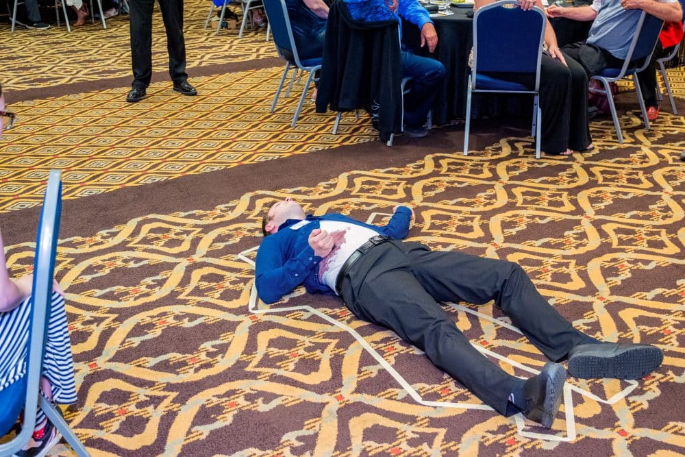 A man lies inside a taped outline on the floor, playfully acting as the “victim” during The Dinner Detective Murder Mystery Show in Louisville.