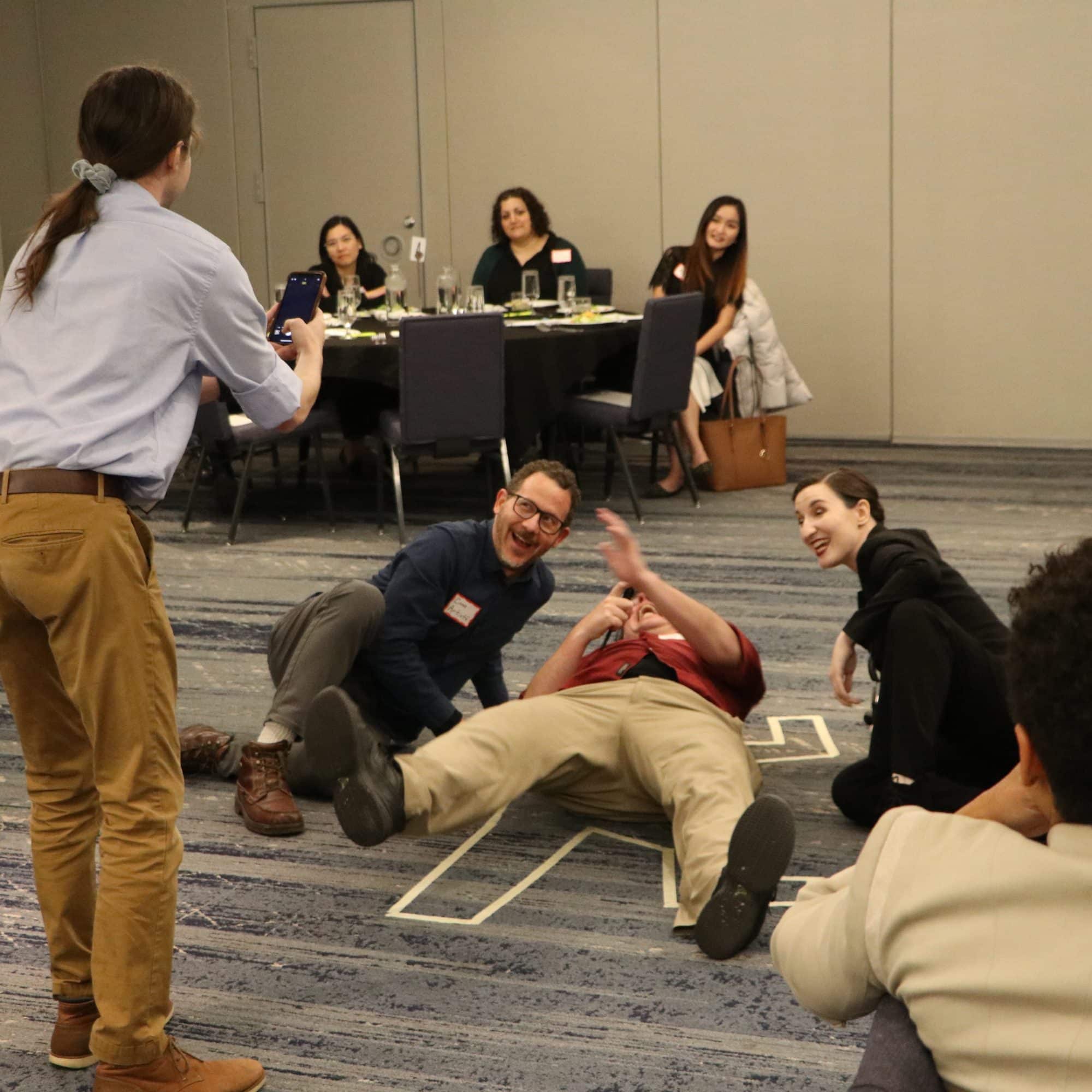 Guests laughing and posing next to a “crime scene” chalk outline during The Dinner Detective Murder Mystery Show in Louisville.