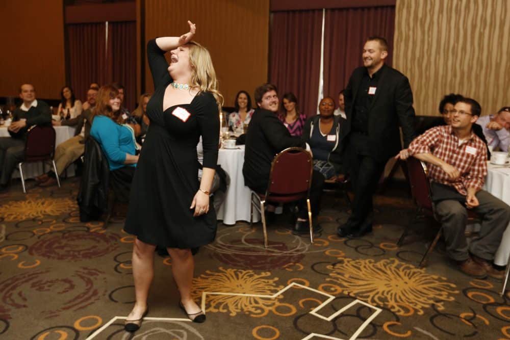 Female guest laughing while participating in an interactive Dinner Detective mystery show, surrounded by amused audience members.