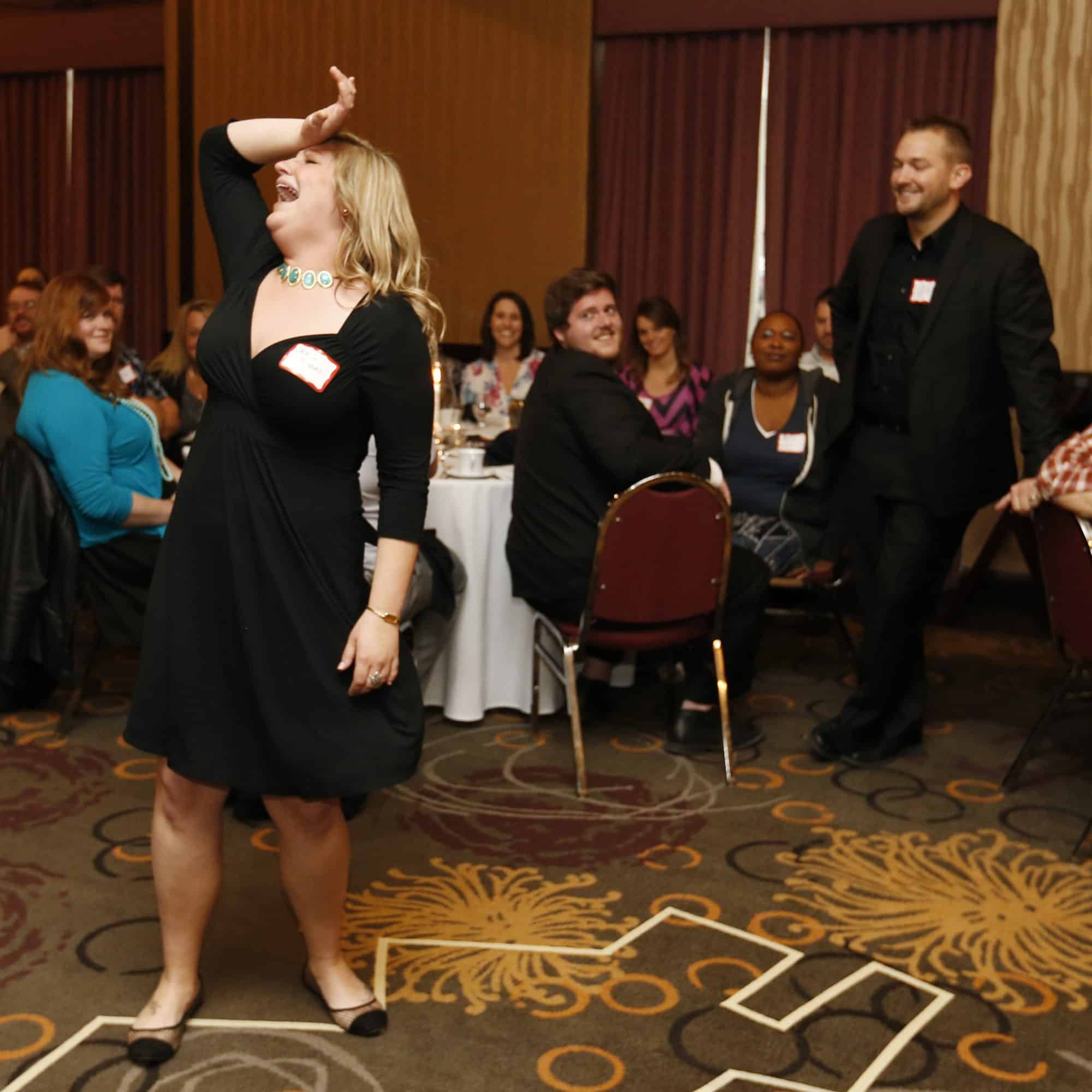 Female guest laughing while participating in an interactive Dinner Detective mystery show, surrounded by amused audience members.