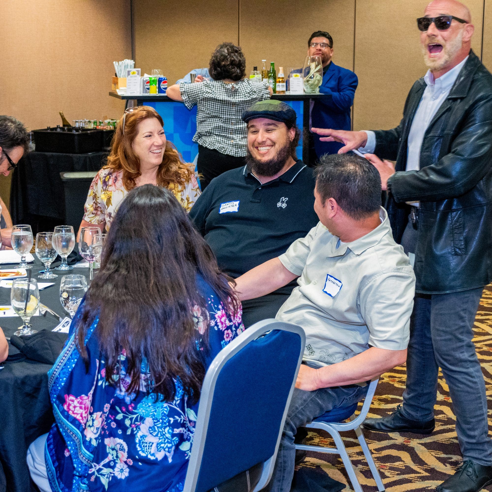 A Dinner Detective performer enthusiastically engages a laughing table of guests during a live murder mystery dinner show.