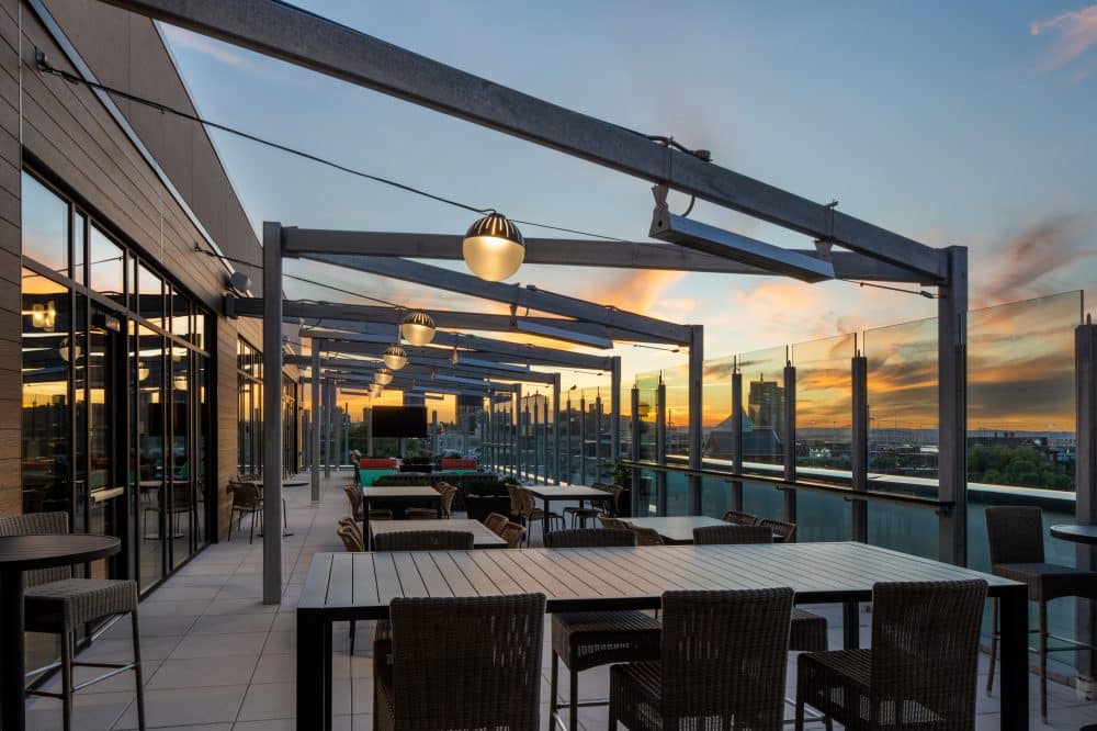 Sunset-lit rooftop terrace at Tempo by Hilton Louisville NuLu, set for evening dining and city skyline views.
