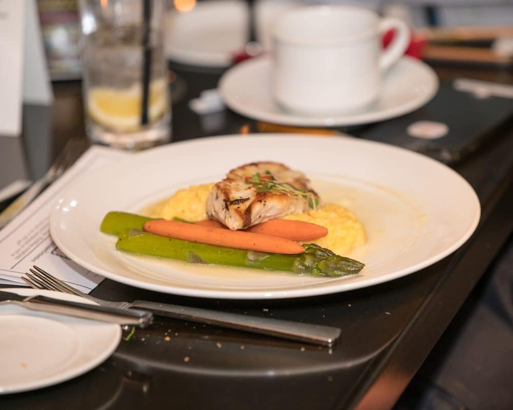 A plated dinner of roasted chicken with polenta, carrots, and asparagus served at The Dinner Detective Louisville.