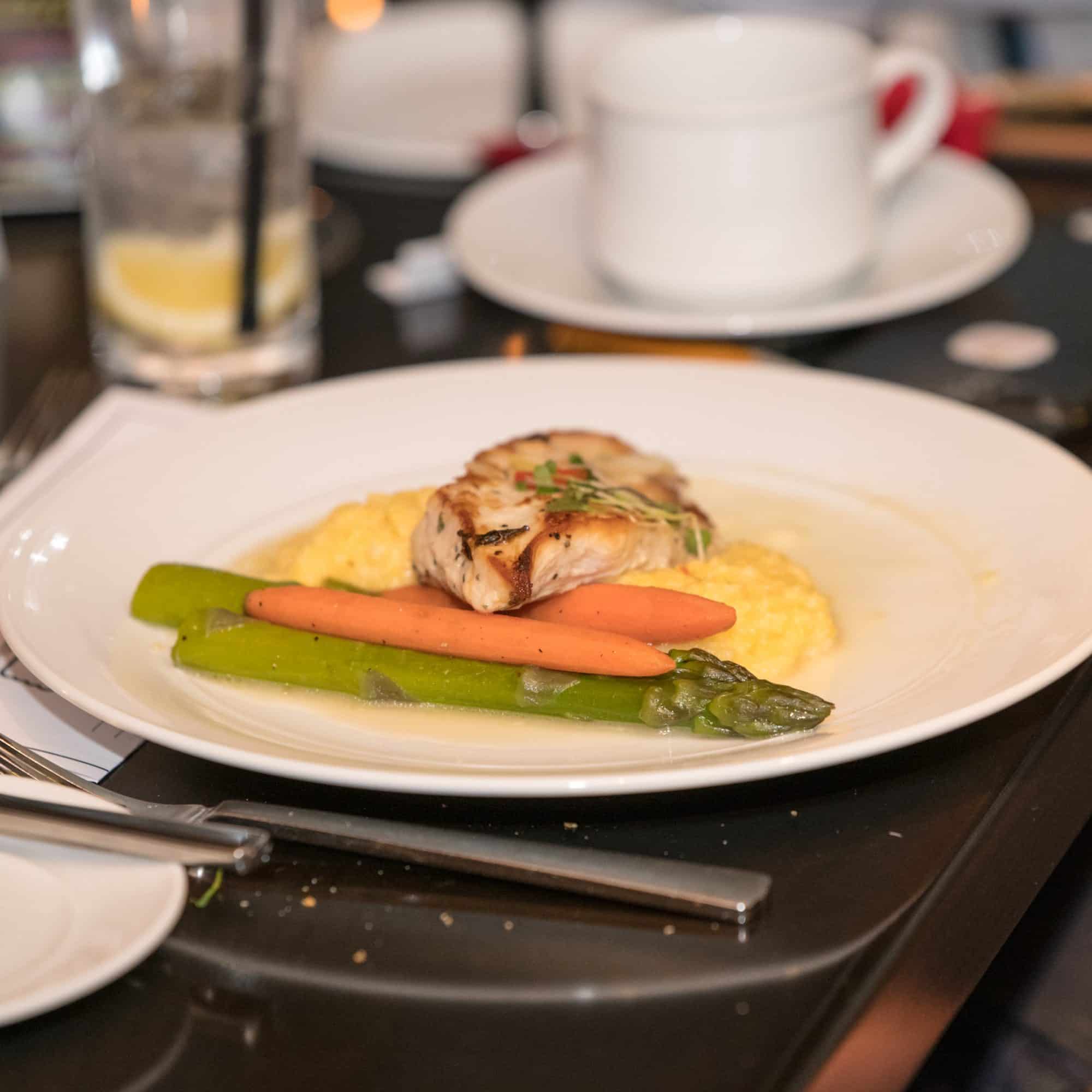 A plated dinner of roasted chicken with polenta, carrots, and asparagus served at The Dinner Detective Louisville.