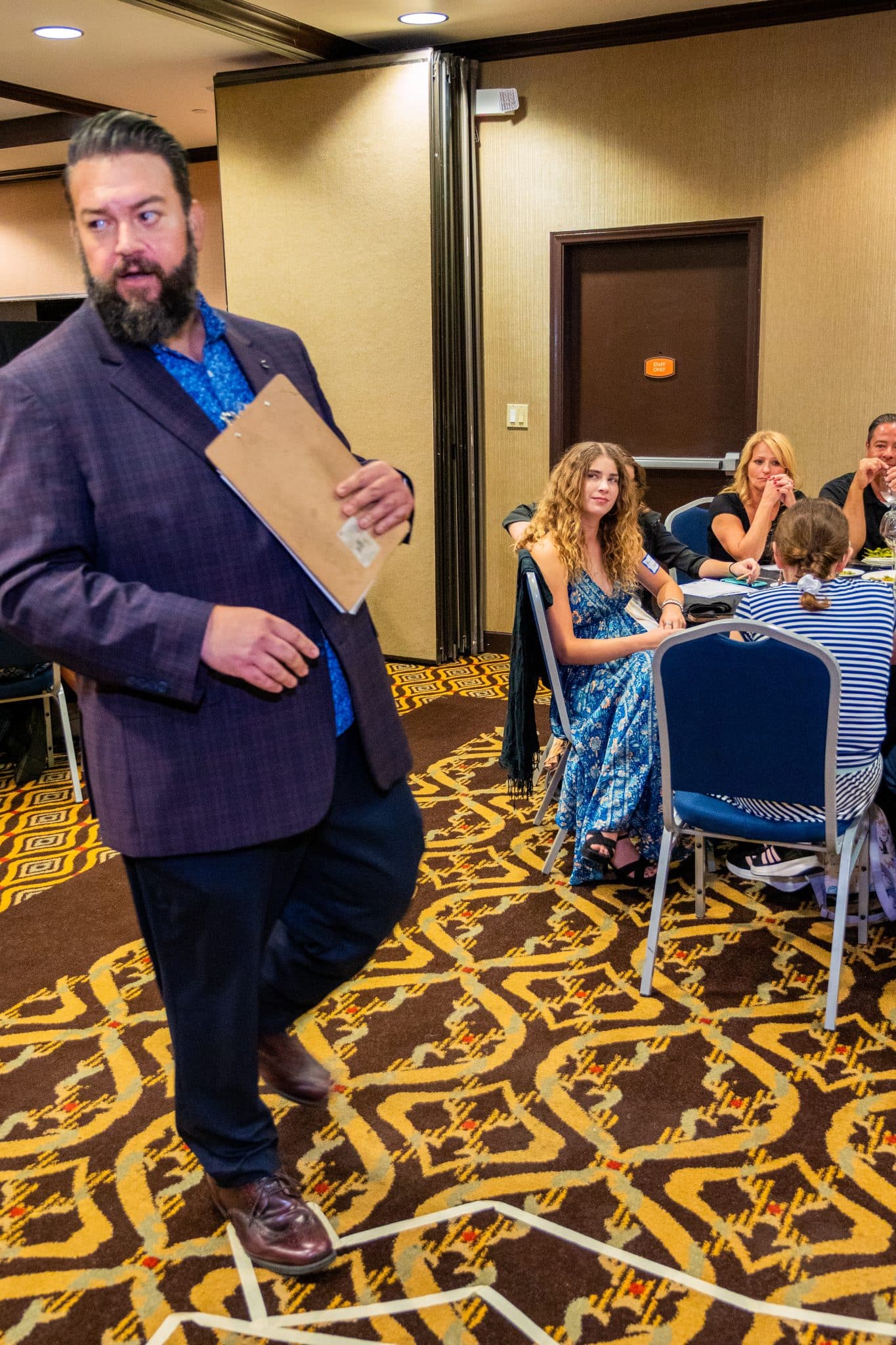 Performer with clipboard engaging audience at Dinner Detective event in a Louisville banquet room.