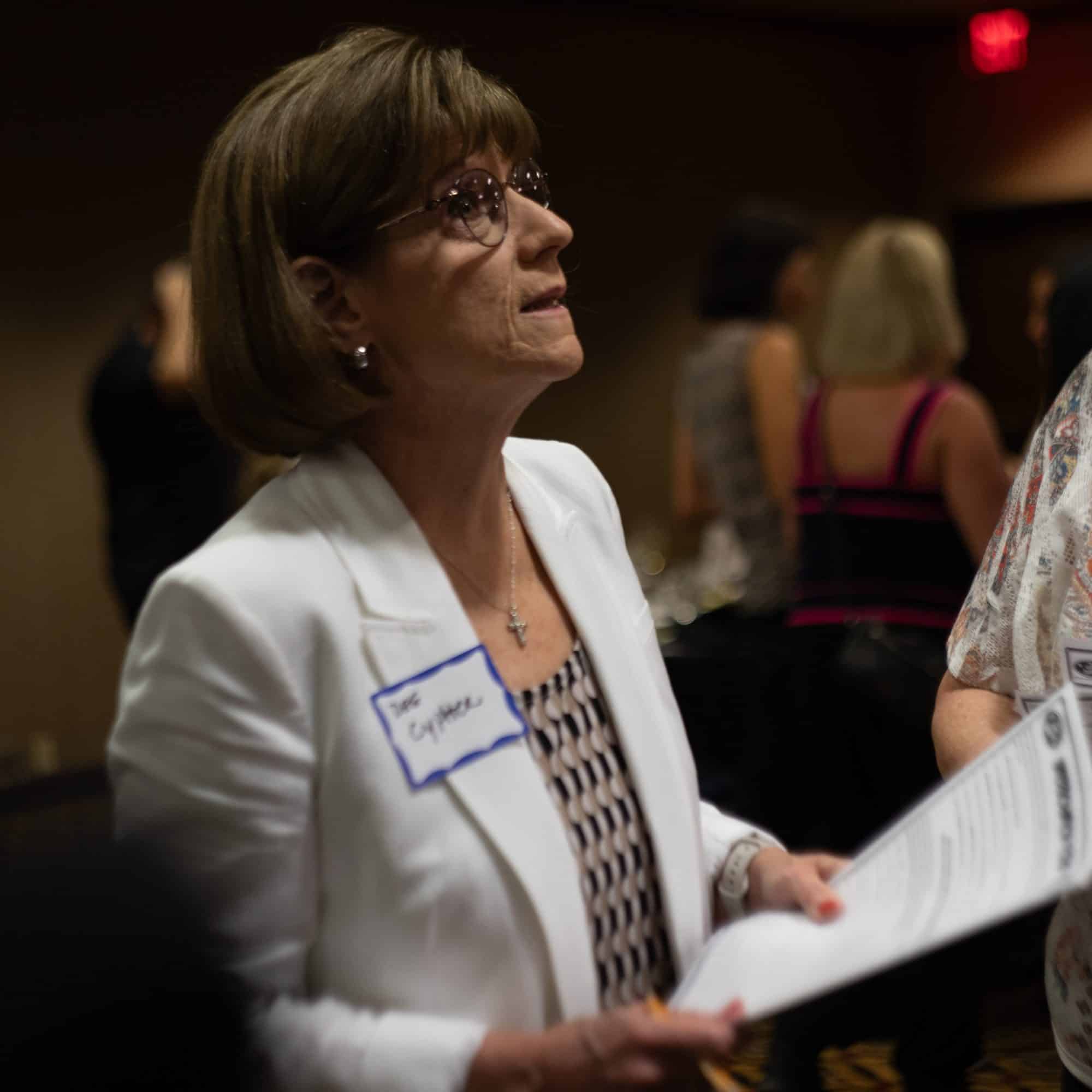 Woman in white blazer reviewing materials during guest interaction at a Dinner Detective event in Louisville.