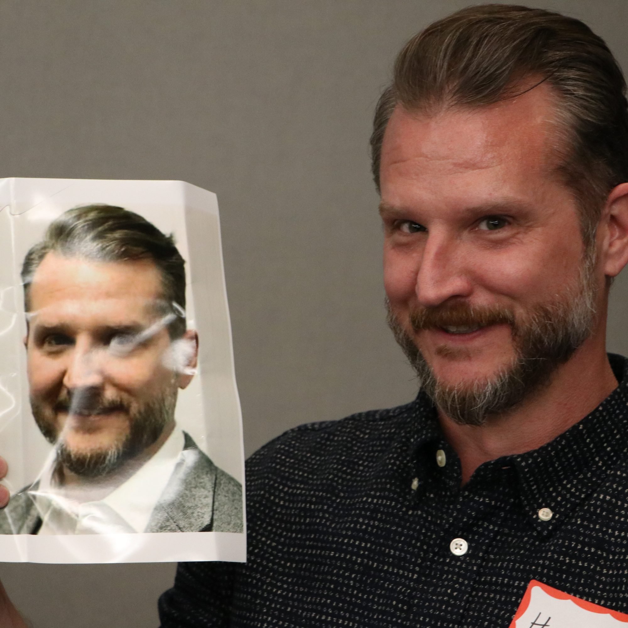 Smiling man holding a photo of himself during a themed Dinner Detective event in Louisville, KY.