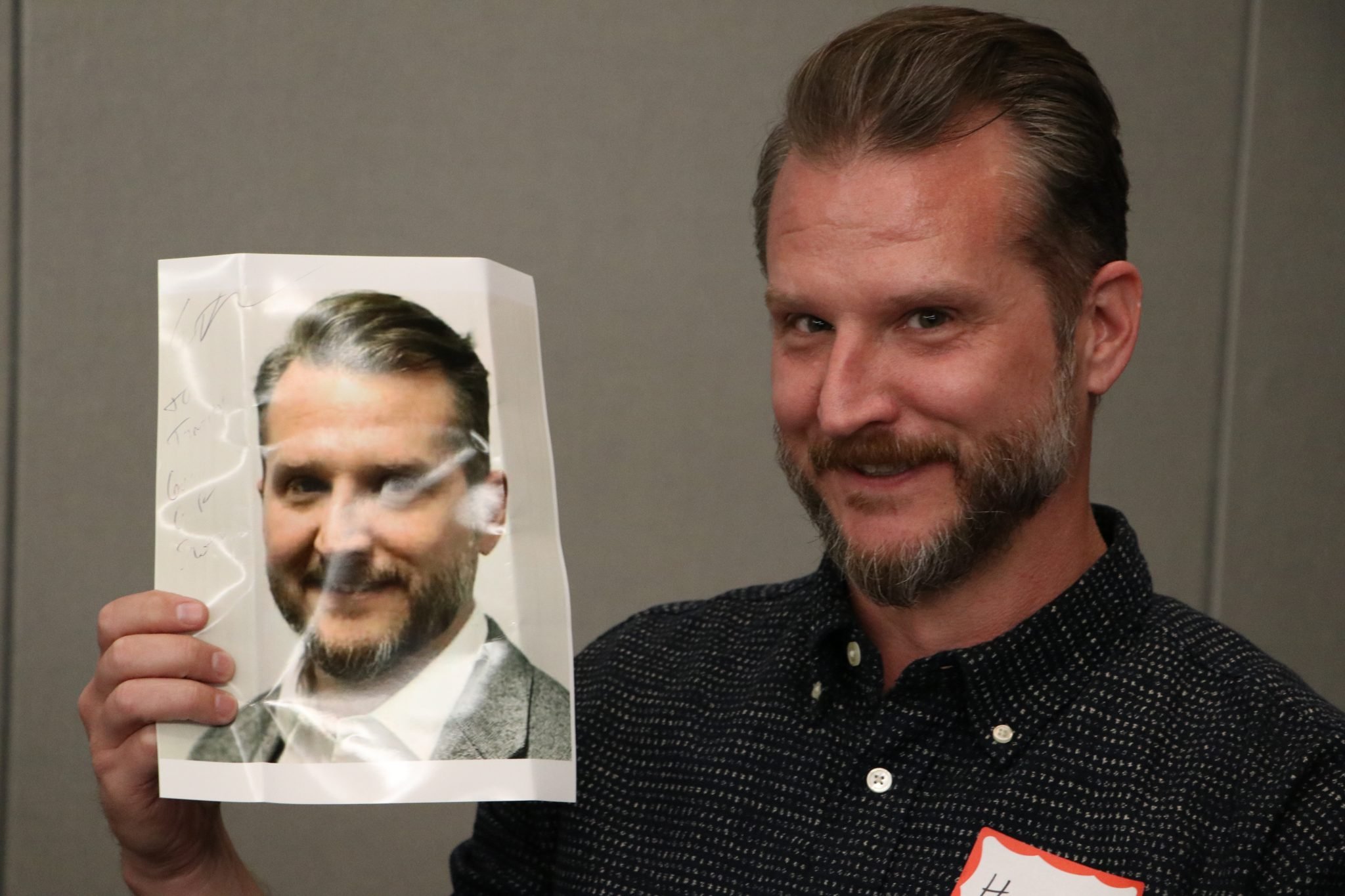 Smiling man holding a photo of himself during a themed Dinner Detective event in Louisville, KY.