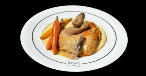 A white plate with roast chicken, two small carrots, okra, and creamy mashed potatoes, arranged neatly on a black background. The plate features an HSG logo at the bottom.