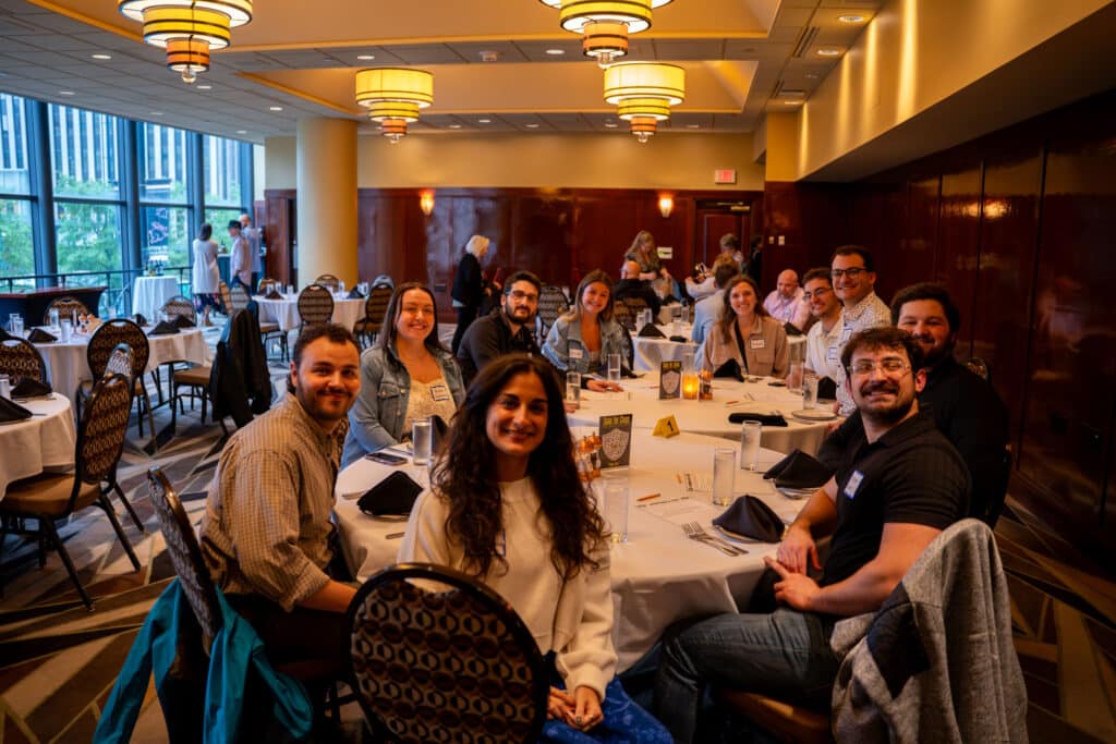 Group seated at a round table smiling before a Dinner Detective murder mystery show in Louisville, with banquet room and city views