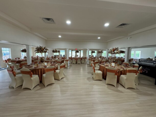 A decorated banquet hall with round tables covered in brown and gold tablecloths, elegant centerpieces, and chairs draped with cream covers and brown sashes, set for a formal event.
