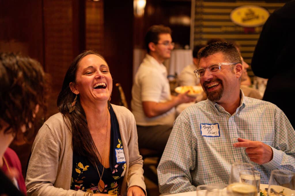 Couple laughing together during The Dinner Detective Portland murder mystery dinner show, enjoying food and interactive entertainment.