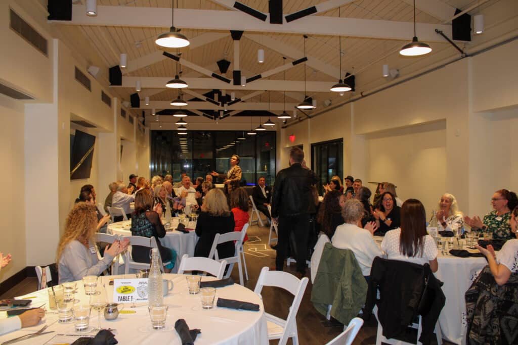 Corporate team laughing during The Dinner Detective murder mystery dinner show in a modern Portland event venue.