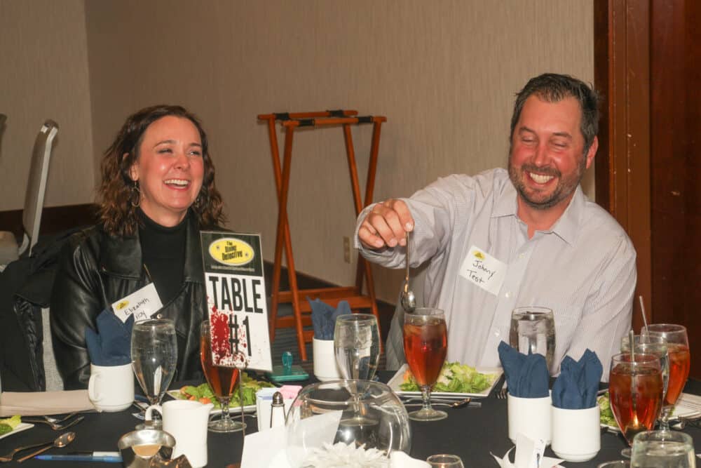 Two smiling guests enjoying dinner at The Dinner Detective Salt Lake City, seated at Table #1 with iced tea and salads.