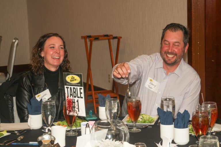 Two smiling guests enjoying dinner at The Dinner Detective Salt Lake City, seated at Table #1 with iced tea and salads.