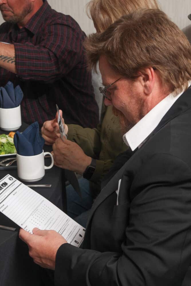 Male guest in formal attire carefully reviewing a clue sheet during The Dinner Detective Salt Lake City dinner show.
