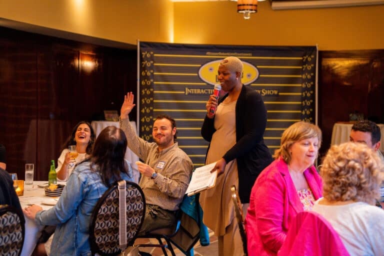 Guest speaks into a microphone during an interactive dinner show in Salt Lake City as the room laughs and follows the case