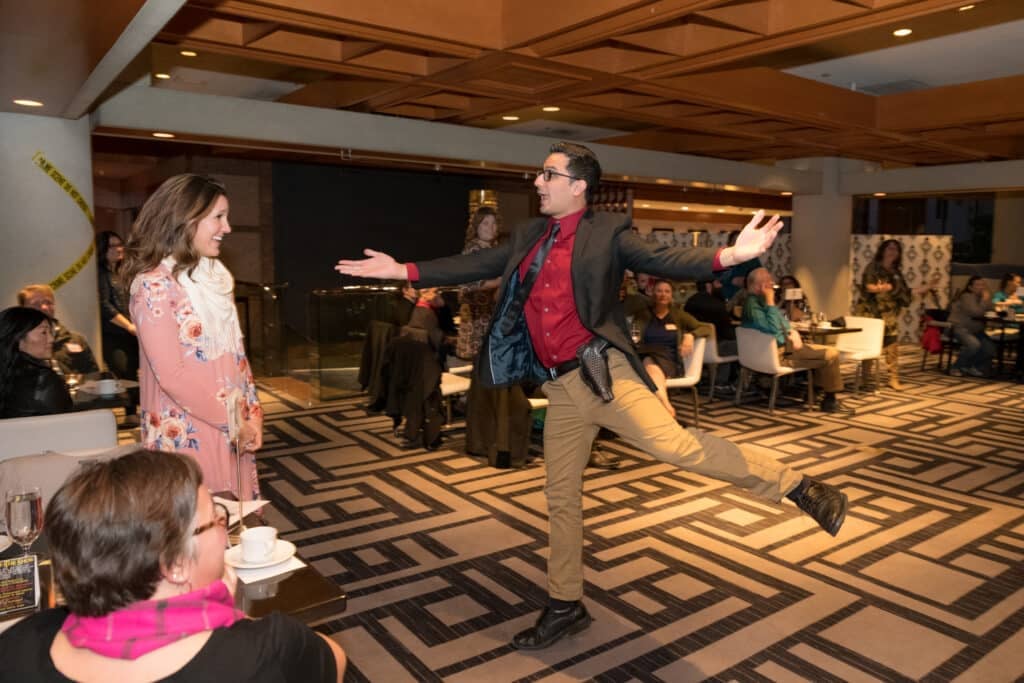 Actor playfully confronts a smiling guest during an interactive dinner show in Salt Lake City as the room watches