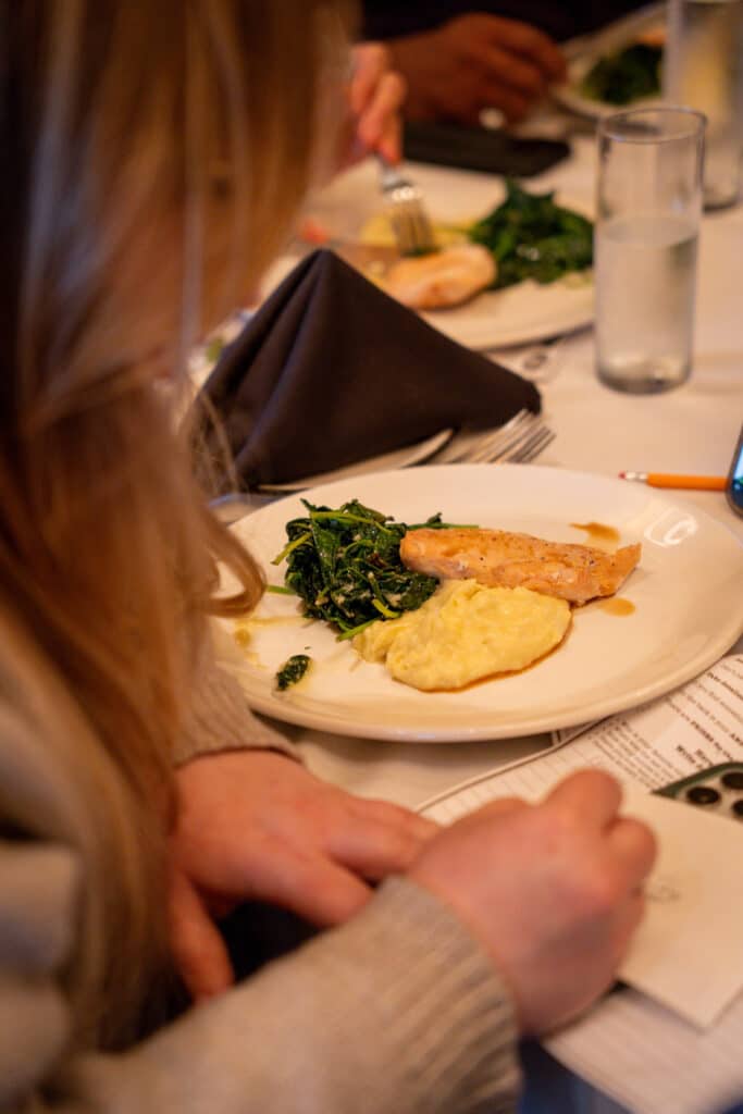Guest enjoying a plated dinner with mashed potatoes, sautéed greens, and grilled chicken at The Dinner Detective event