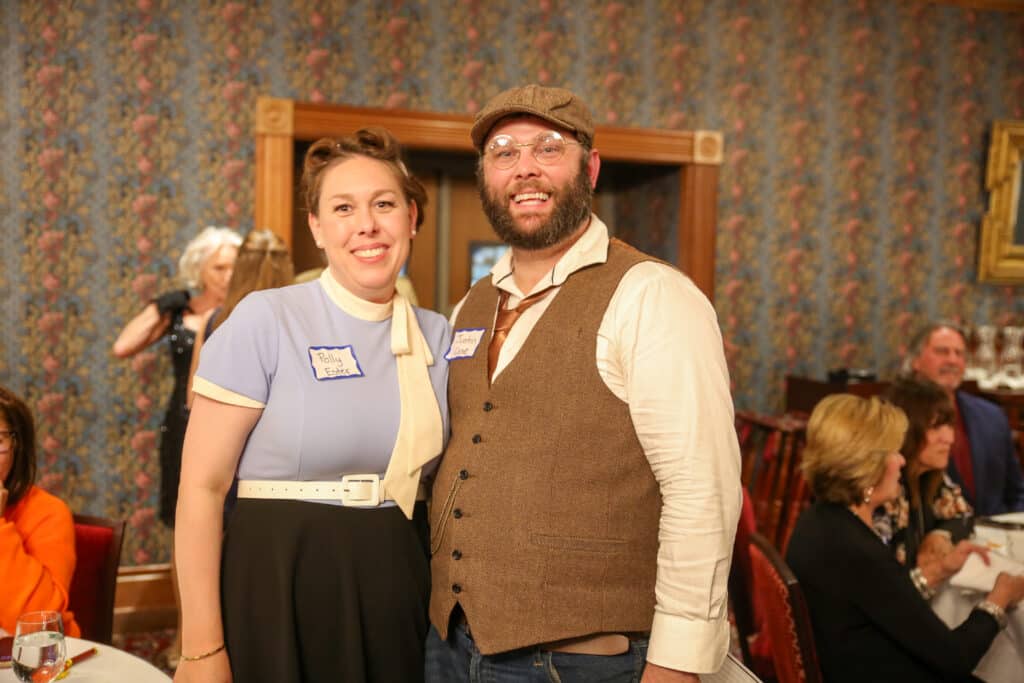 Couple in playful costumes with pun name tags posing at a Dinner Detective mystery dinner.