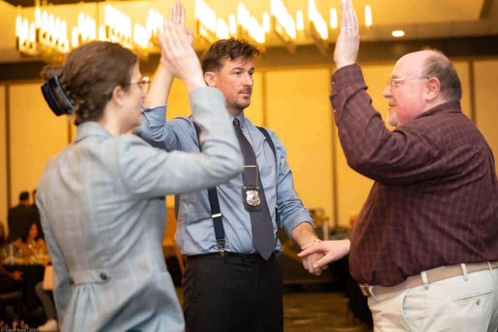 Guests high-fiving a detective character during an interactive Dinner Detective mystery show.