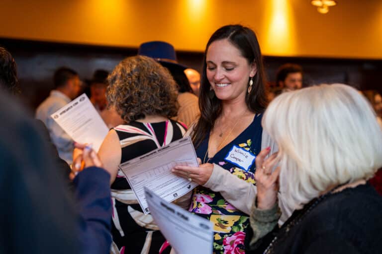 A woman with a "Winnie Cooper" name tag smiles while reviewing an evidence sheet during a Dinner Detective interactive event in San Francisco.