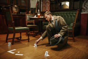 A detective in a trench coat examines evidence markers on the wooden floor of a vintage room. Amidst true crime whispers, a green upholstered bench and a round table with a bottle and card hint at mysteries unsolved.