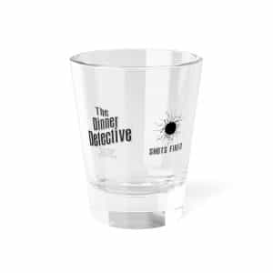 A clear Shot Glass features The Dinner Detective and SHOTS FIRED, adorned with a black bullet hole graphic.