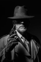 A black-and-white image of a mysterious detective wearing a wide-brimmed hat and trench coat, holding a revolver. His face is partially obscured by shadow, creating an enigmatic atmosphere reminiscent of what makes a good detective in classic noir stories.